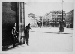 Combattimenti in Piazza Goldoni a Trieste il 30 aprile 1945, con due uomini armati al riparo all'angolo di un edificio.