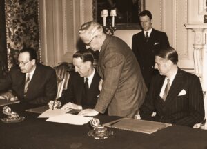 Cerimonia diplomatica a Londra nel 1954: un rappresentante firma un documento alla presenza di altri funzionari, in occasione del Memorandum d'intesa su Trieste.