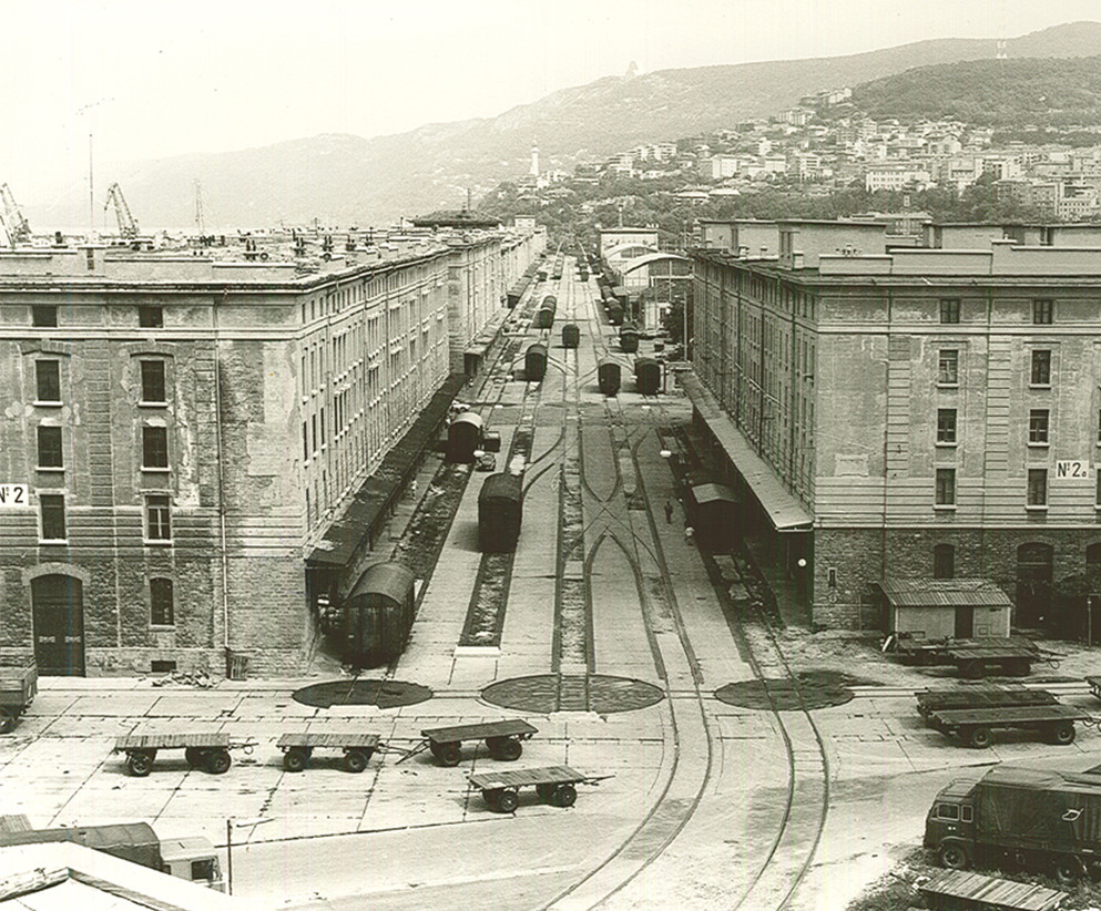 Fotografia storica in bianco e nero del Porto Vecchio di Trieste, con moli, banchine e magazzini portuali.